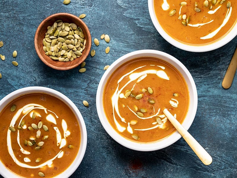 This flavorful and easy pumpkin soup takes less than 30 minutes to make and is the perfect simple side for a gooey grilled cheese sandwich! BudgetBytes.com Three bowls of Easy Pumpkin Soup garnished with sour cream and pepitas, a small bowl of pepitas on the side.