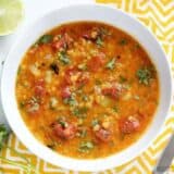 Above view of Mexican red lentil stew in a bowl alongside lime and coriander.