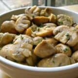 Bowl of marinated mushrooms with herbs.