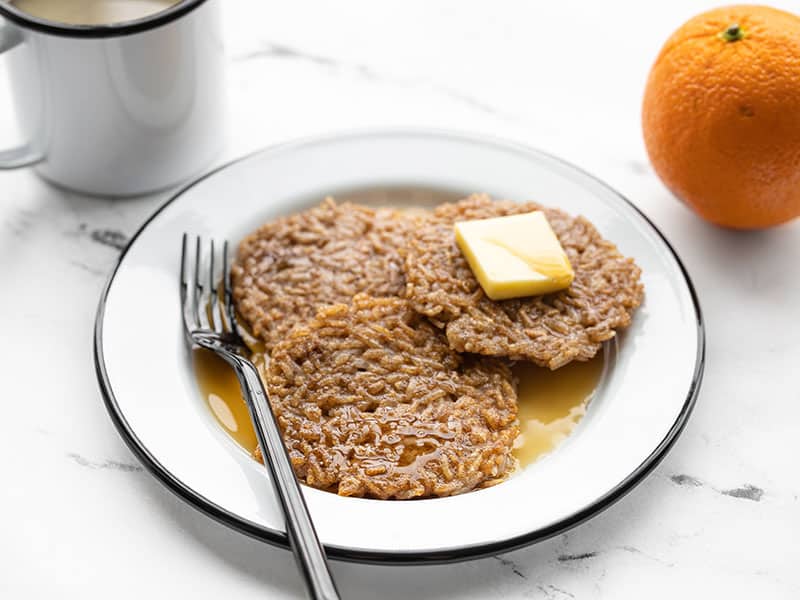 Use your leftover rice from the night before to make these quick and easy Rice Pancakes for breakfast. Reduce food waste and keep your budget in check! BudgetBytes.com Front view of rice pancakes on a plate with butter and maple syrup, an orange and cup of coffee in the back