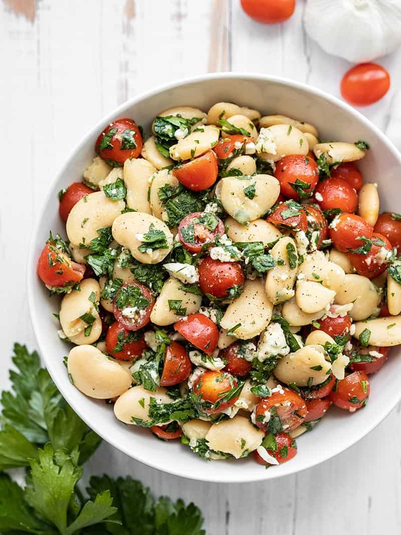 A big bowl full of Mediterranean White Bean Salad with tomatoes and parsley on the side