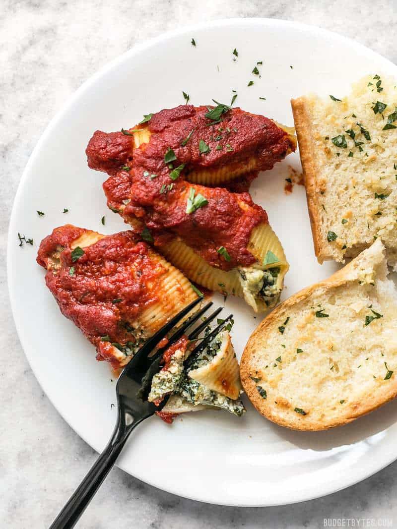 These easy Pesto Stuffed Shells are stuffed with two cheeses, pesto, and spinach. Perfect for meal prep or freezing portions for later! Pesto Stuffed Shells served on a plate with garlic bread.
