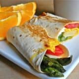 Asparagus breakfast wraps with cream cheese filling on a plate with oranges.