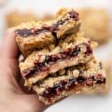 A hand holding a stack of raspberry oatmeal bars close to the camera
