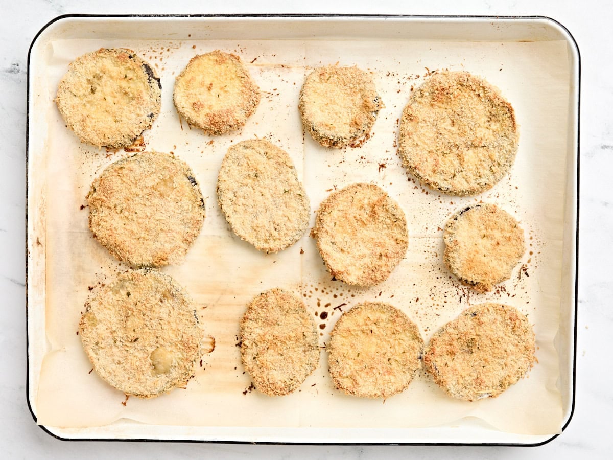 Breaded parmesan slices on a parchment lined baking sheet.
