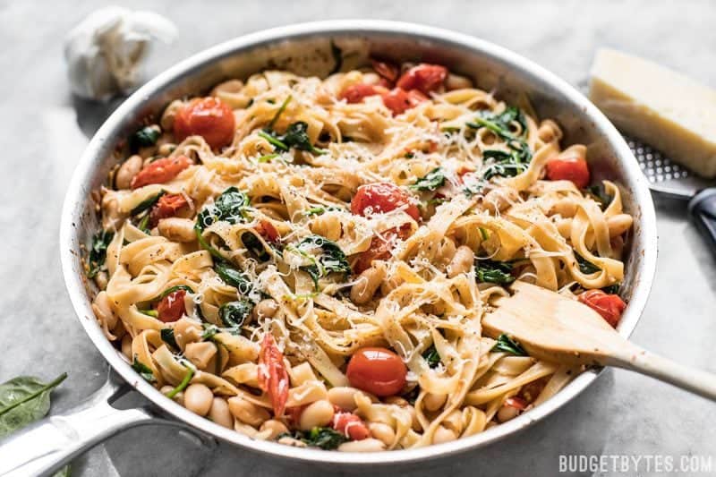 This Tuscan White Bean Pasta is a fast and flavorful dish that is perfect for weeknight dinners. Caramelized garlic, basil, and Parmesan add BIG flavor! Budetbytes.com Tuscan white bean pasta in the skillet with a wooden pasta fork in the side
