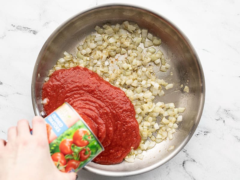 Crushed tomatoes being poured into the skillet.