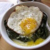 Plate of grits topped with greens and herbs served with a fork.