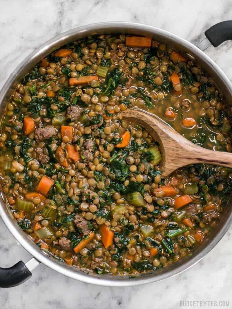 Lentil & Sausage Stew is a fast and easy soup bursting with flavor and chock full of good-for-you vegetables! Plus it freezes well for later. BudgetBytes.com Lentil & Sausage Stew in pot with wooden spoon