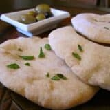 Whole pita bread displayed on a wooden board.