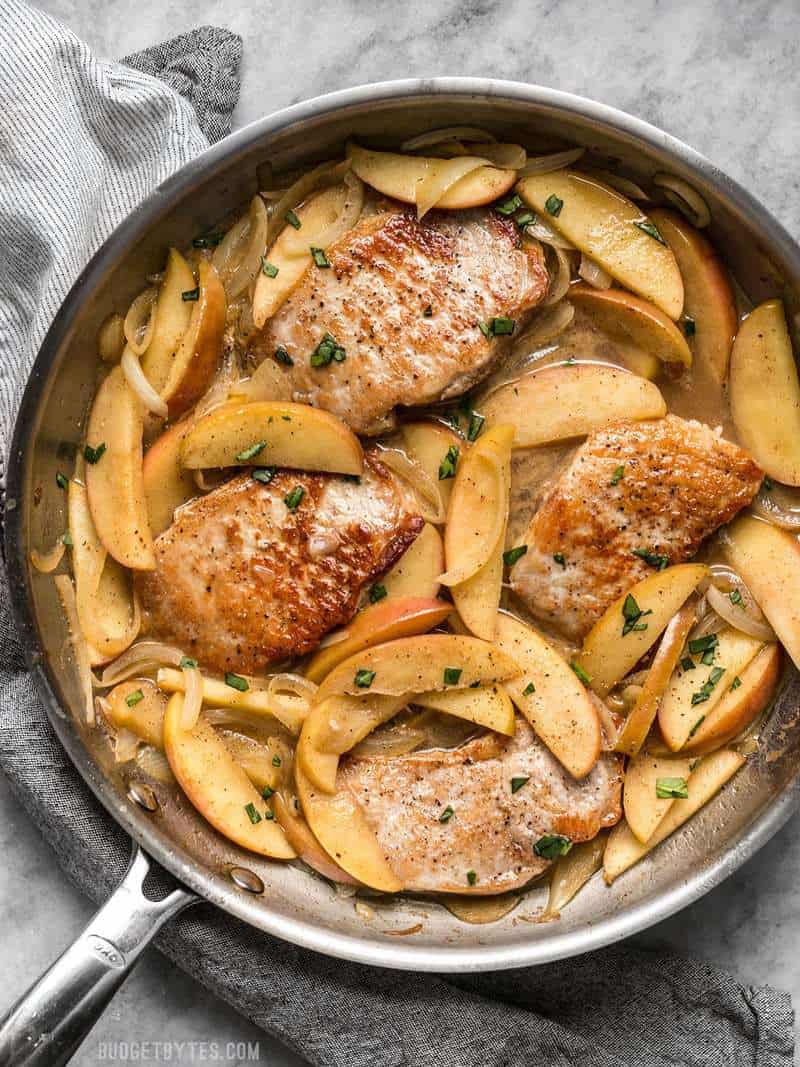 A skillet full of Apple Spice Pork Chops with parsley sprinkled over top