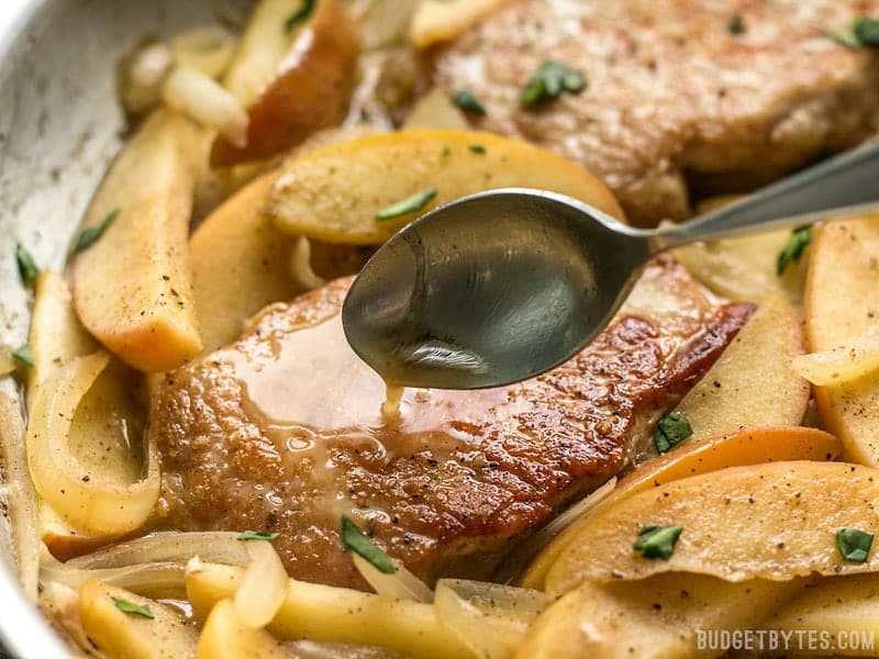 These Apple Spice Pork Chops are smothered with apples, onions, cinnamon, and a buttery pan sauce that is sweet, salty, and rich. Budgetbytes.com Pan sauce being drizzled over Apple Spice Pork Chops in the skillet