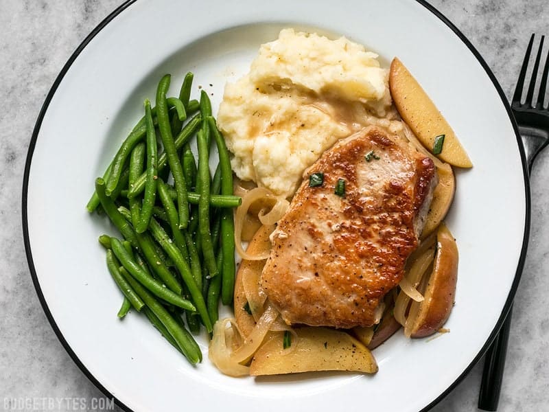 This Apple Spice Pork Chop meal prep is packed with tender and juicy pork chops, creamy mashed potatoes, and bright green beans. BudgetBytes.com Apple Spice Pork Chops, Instant Pot Mashed Potatoes, and green beans on a plate