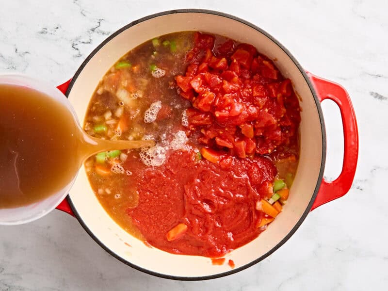 Canned chopped tomatoes, tomato sauce, and beef broth added to a pot of mirepoix.