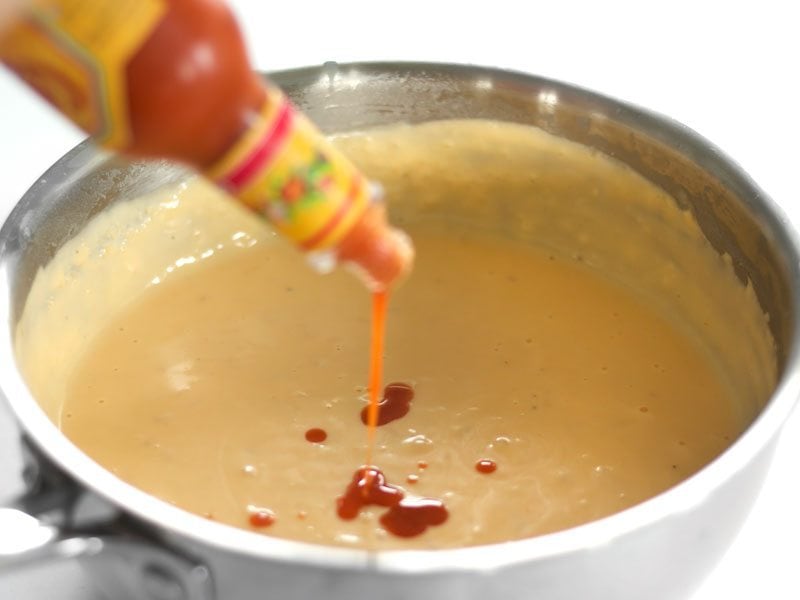 Hot sauce being poured into cheese sauce mixture