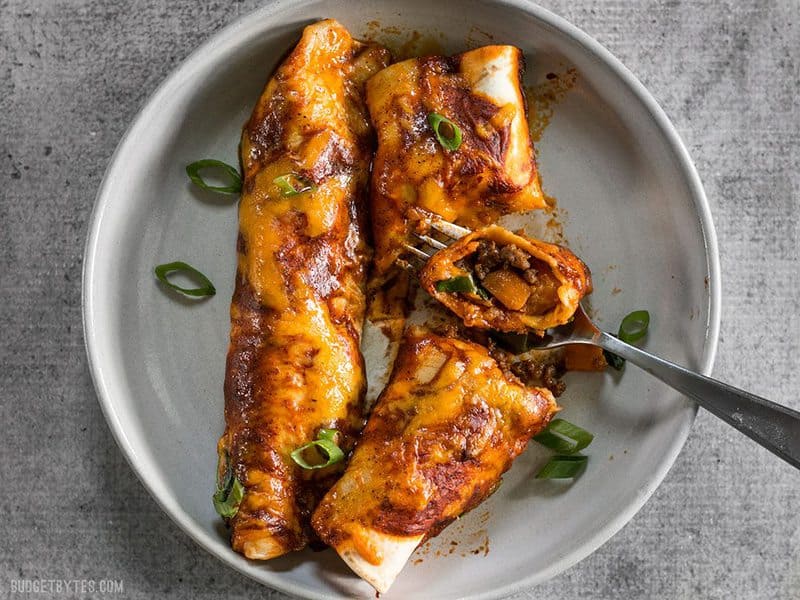 These award winning Chorizo and Sweet Potato enchiladas have a perfectly balanced sweet and spicy flavor that will leave you wanting more. BudgetBytes.com Two Chorizo and Sweet Potato enchiladas on a plate being eaten with a fork