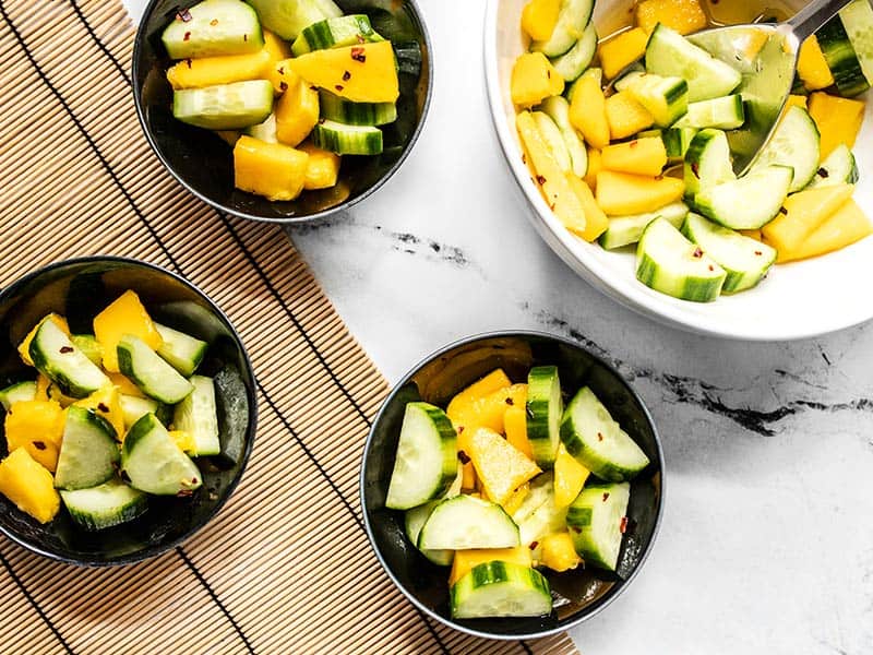 Fresh cucumber and tropical mango come together with a sweet and spicy dressing to make this light and refreshing Cucumber Mango Salad. Budgetbytes.com Cucumber mango salad being served into small black bowls from the large white bowl.