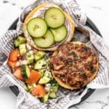 Overhead view of an open faced Mediterranean Turkey Burger on a paper lined plate with cucumber salad on the side