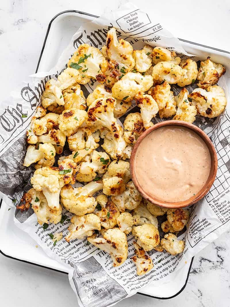 Garlic parmesan roasted cauliflower is an easy, flavorful side dish or snack that will have everyone begging for seconds. Budgetbytes.com Overhead of Garlic Parmesan Roasted Cauliflower on a tray with a bowl of dipping sauce