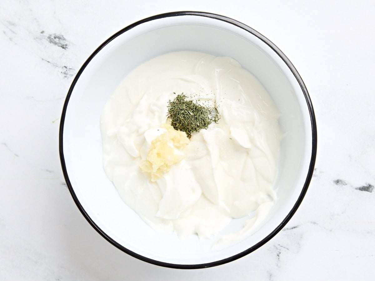 The ingredients to make a herb yogurt sauce in a mixing bowl.
