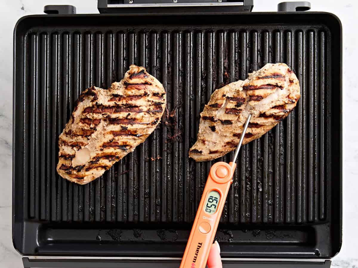An internal thermometer checking the temperature of a grilled chicken breast.