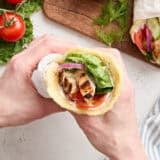 Overhead view of a pair of hands holding a chicken shawarma wrap.