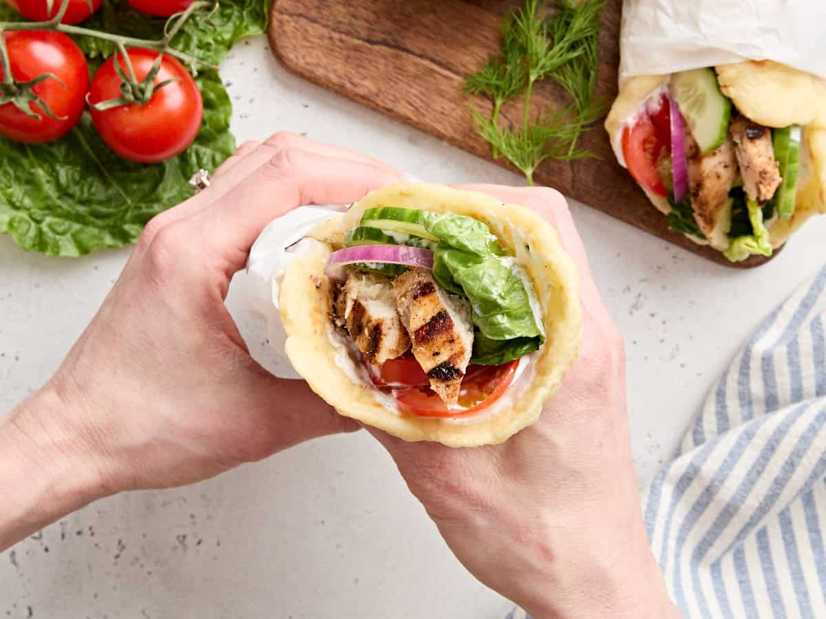 Overhead view of a pair of hands holding a chicken shawarma wrap.