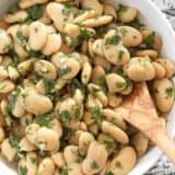 Close-up of marinated white beans in a bowl with a wooden spoon.