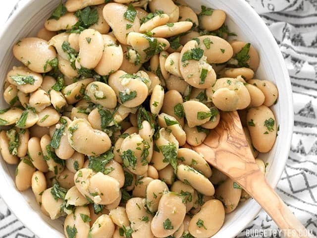 Top view of Marinated White Beans in white bowl with wooden serving spoon