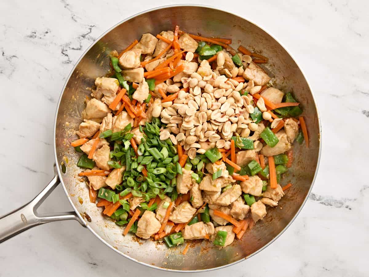Sliced green onions and peanuts added to kung pao chicken in a skillet.