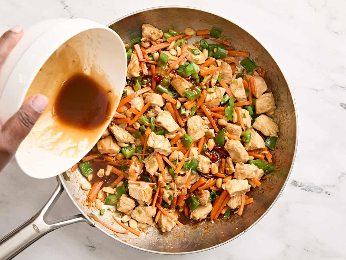 Sauce being added to homemade kung pao chicken in a skillet.
