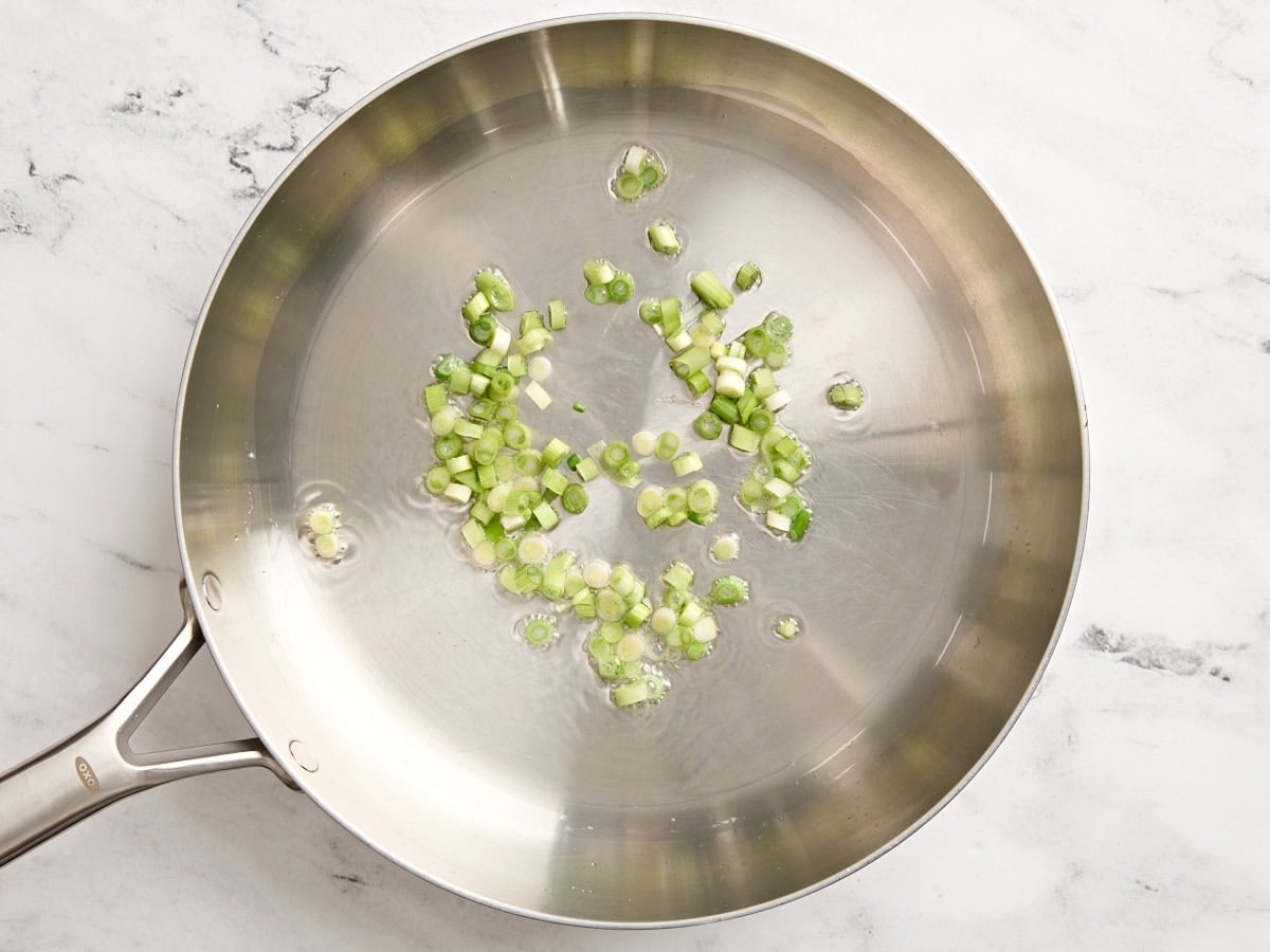 Sliced green onions sauteeing in a skillet.