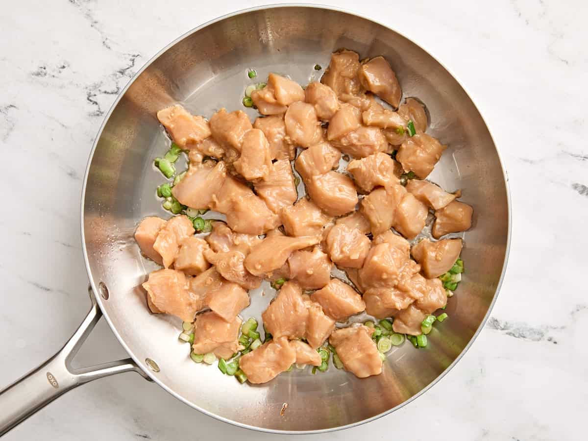 Kung pao chicken in a skillet with green onions.