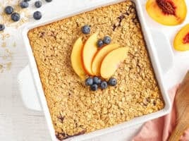 Overhead view of a baking dish of baked oatmeal topped with peach slices and blueberries.