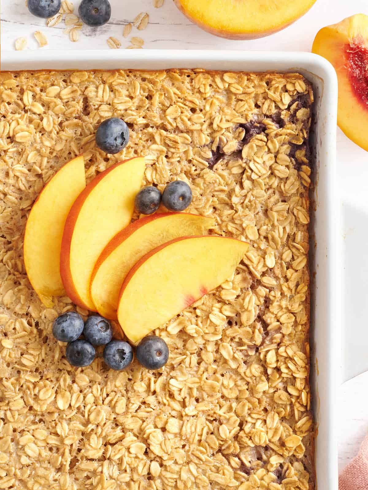 Overhead close up of a baking dish with baked oatmeal topped with peach slices and blueberries.