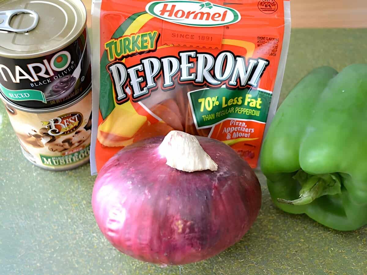 A red onion, packet of pepperoni, a can of olives, and a green bell pepper.