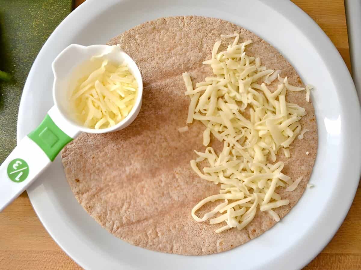 A tortilla topped with shredded cheese.