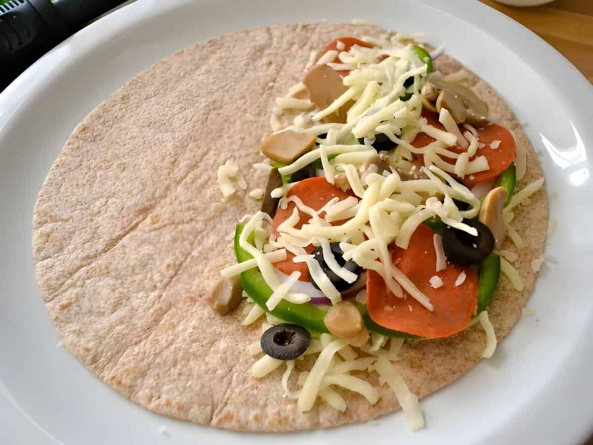 A tortilla topped with shredded cheese and pizzadilla toppings.