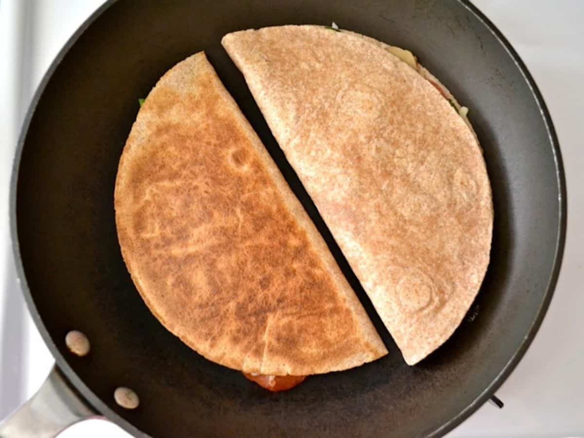 Two pizzadillas cooking in a skillet.