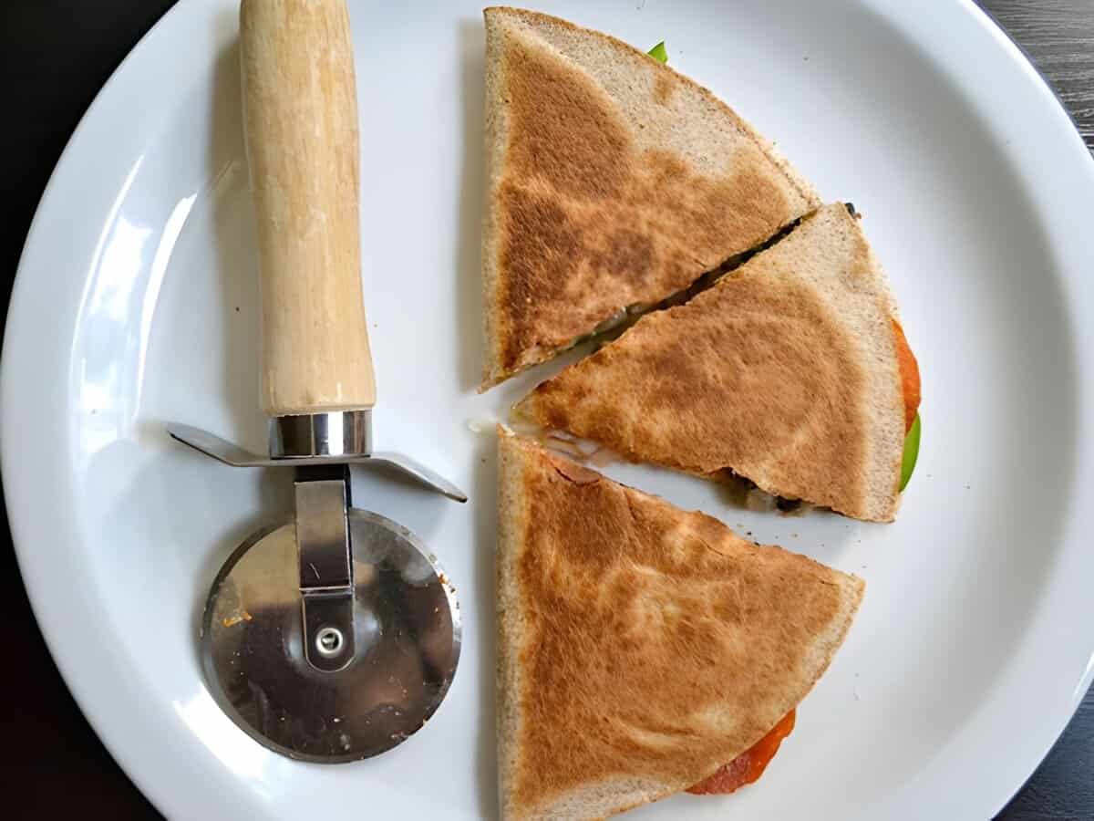 A pizzadilla sliced into three triangles on a plate with a pizza cutter.