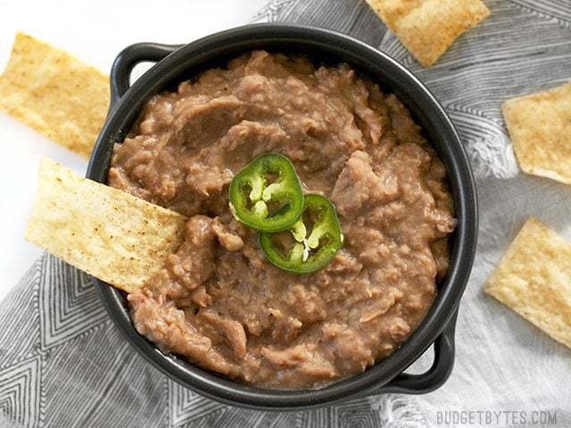 Use your slow cooker to make these incredibly flavorful (not) refried beans with next to no effort. They're versatile, delicious, and freezer friendly. Budgetbytes.com A chip being dipped into a bowl of slow cooker (not) refried beans with jalapeño garnish