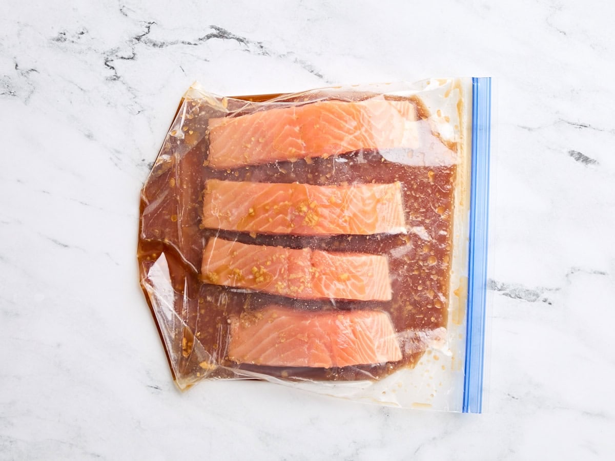 Raw salmon fillets marinating in a bag of teriyaki sauce marinade.