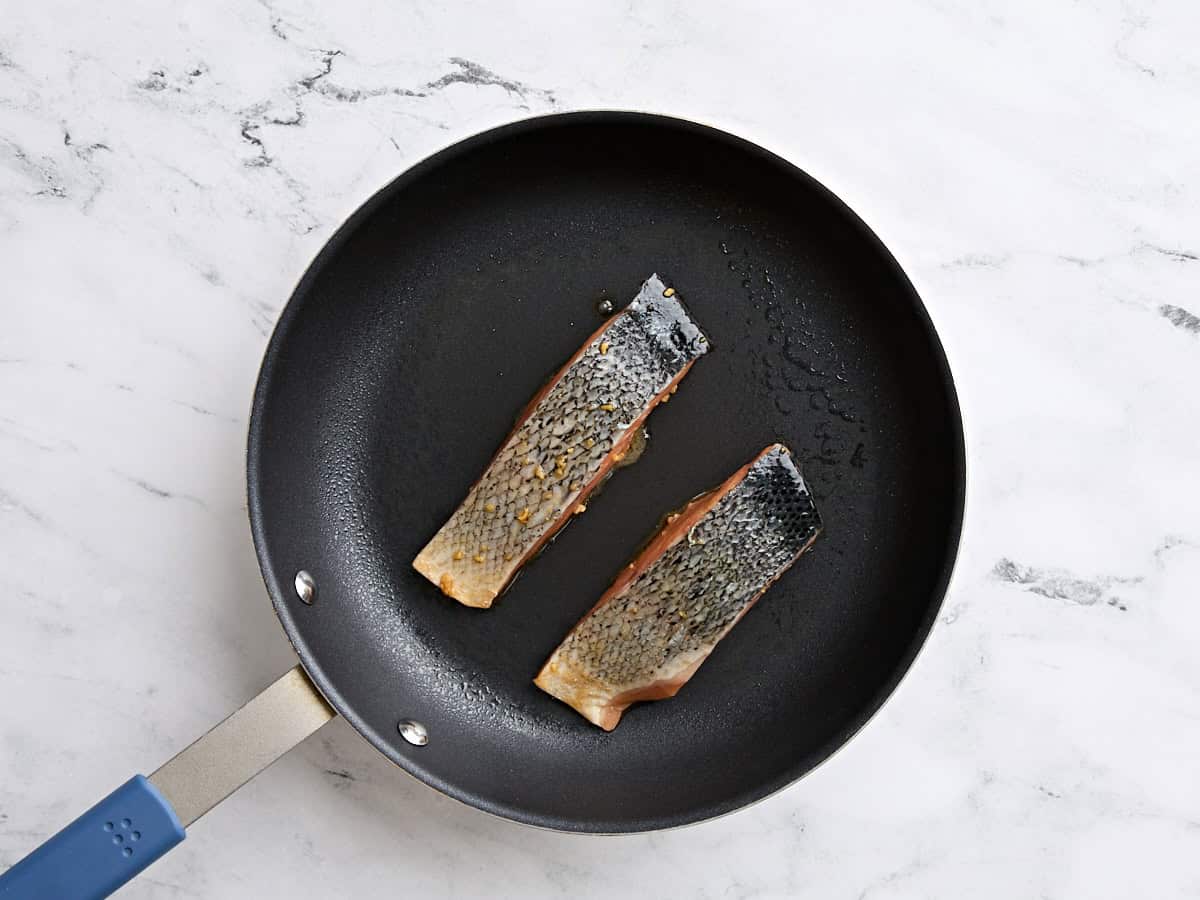 Teriyaki salmon fillets cooking in a skillet.