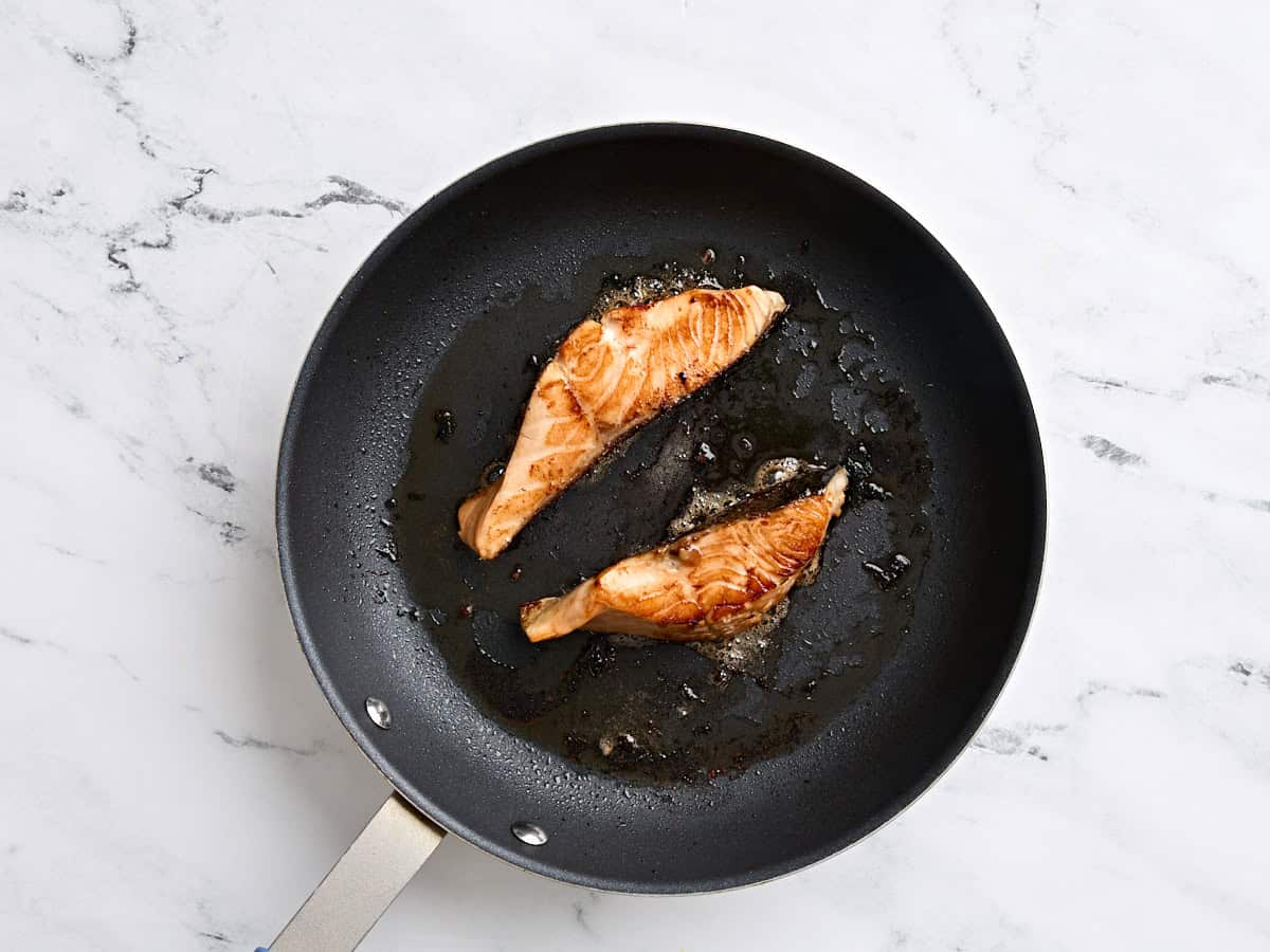 Teriyaki salmon fillets cooking in a skillet.