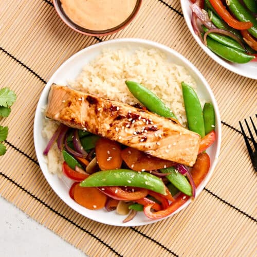 Overhead view of teriyaki salmon on a plate with stir fried vegetables and rice.
