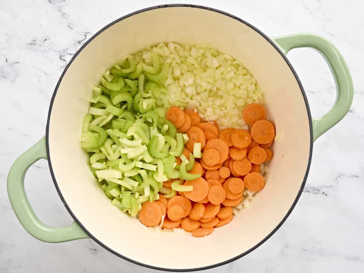 Celery and carrots added to sauteed onion and garlic in a pot.