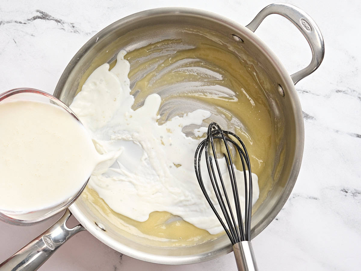Milk being whisked into a roux in a skillet.