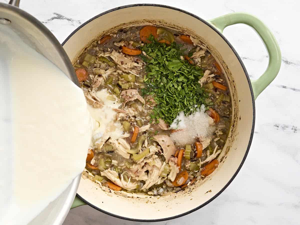 Cream sauce being poured into a pot of chicken and rice soup.