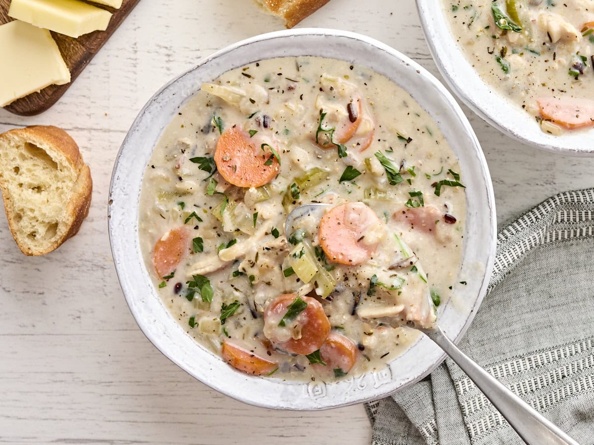 Overhead view of a bowl of creamy chicken and rice soup with a spoon taking some.