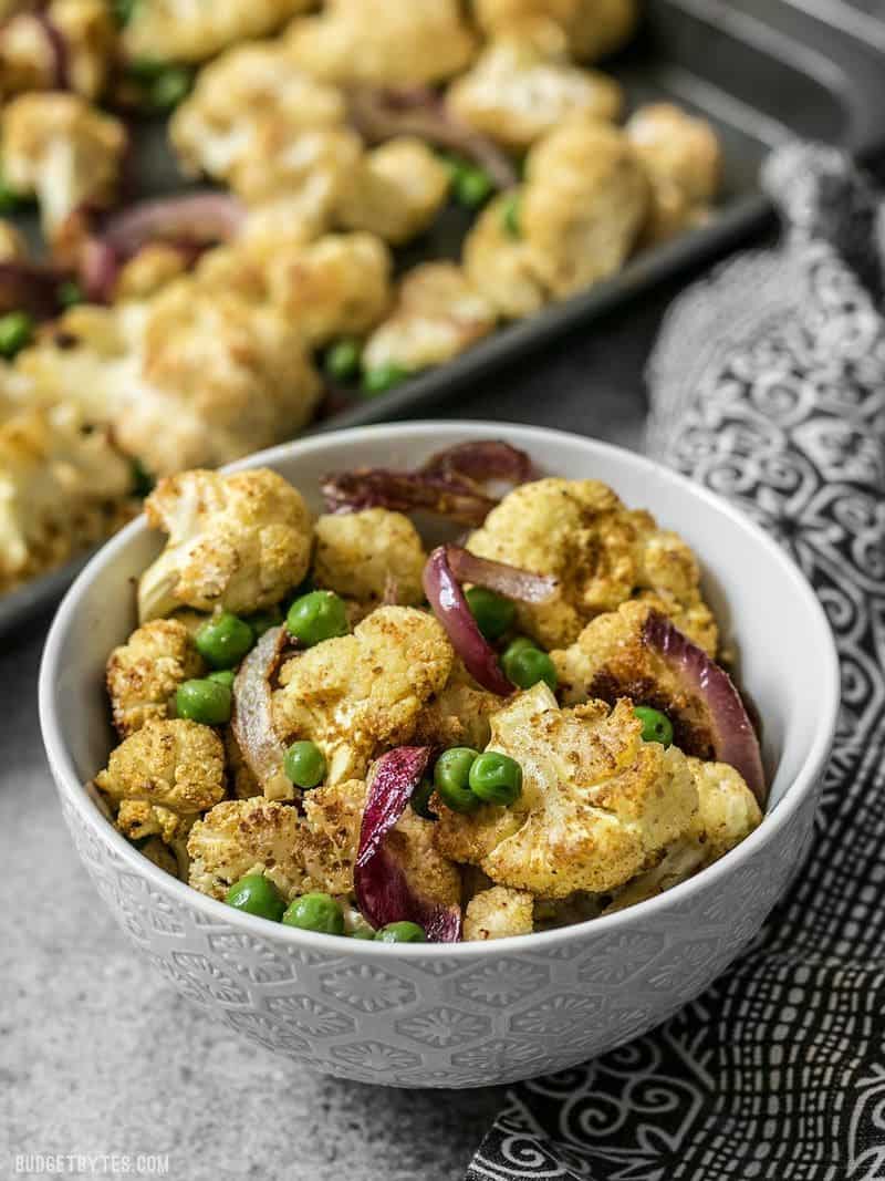 Curry Roasted Cauliflower is an easy way to turn boring cauliflower into a vibrantly spiced side dish with just a few ingredients. Budgetbytes.com A bowl of Curry Roasted Cauliflower with the sheet pan behind it.
